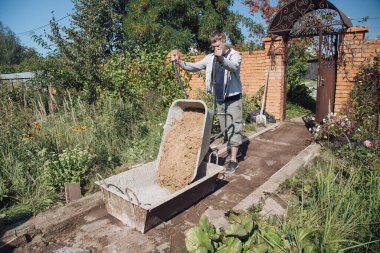 Bir adam çimento karışımına kum boşaltır bahçe yolu dökerek, bahçe arazisinde inşaat yapar.