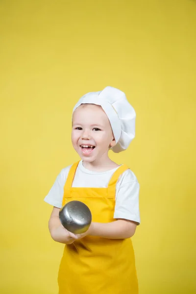 扮演厨师的小高加索男孩 穿着围裙的男孩和戴着厨师帽子的男孩在黄色背景下的情感姿势 — 图库照片