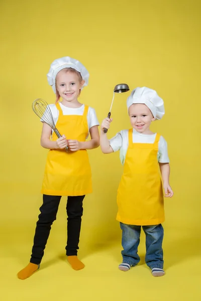 扮演厨师的孩子们 穿着围裙 头戴厨师帽的男孩和女孩们都站在黄色的背景上 — 图库照片