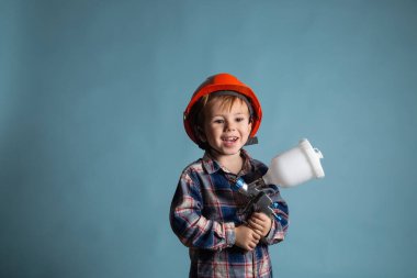 Kafkasya şapkalı, elinde elektrikli sprey tabanca, boyacı ya da dekoratör konsepti olan şirin beyaz bir çocuk..