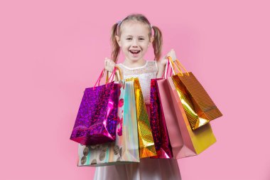Pembe arka planda izole edilmiş alışveriş torbalarıyla parti elbisesi giymiş komik beyaz bir kız..