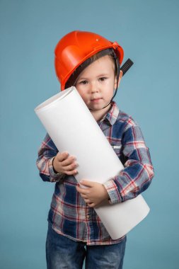 Kafkaslı şirin beyaz çocuk müteahhitin portresi. Elinde mavi arka planda inşaat tasarımı var. Mutlu bir aile için ev yapma fikri