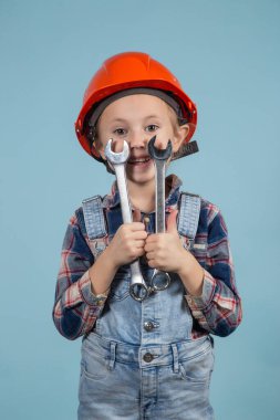 Mavi arka planda komik poz veren turuncu şapkalı şirin bir kız. İki elinde de İngiliz anahtarı var. İnşaat ve onarım konsepti.