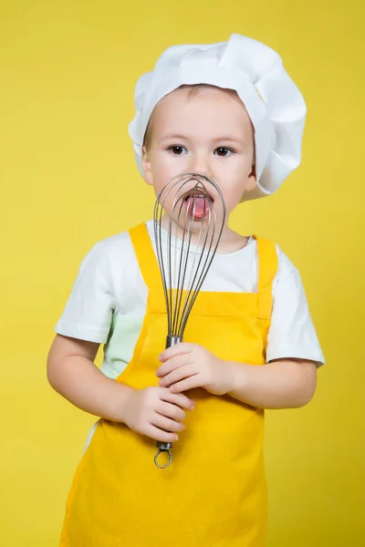小高加索男孩在扮演厨师 男孩在围裙和厨师的帽子拿着威士忌在黄色背景下鞭打奶油 — 图库照片