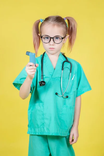 穿着医生绿色外套 手里拿着哮喘吸入器 背景为黄色的高加索小女孩的画像 — 图库照片