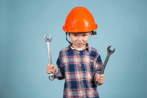 A cute funny little boy in an orange hard hat posing funny, holding wrenches — Stock Photo, Image