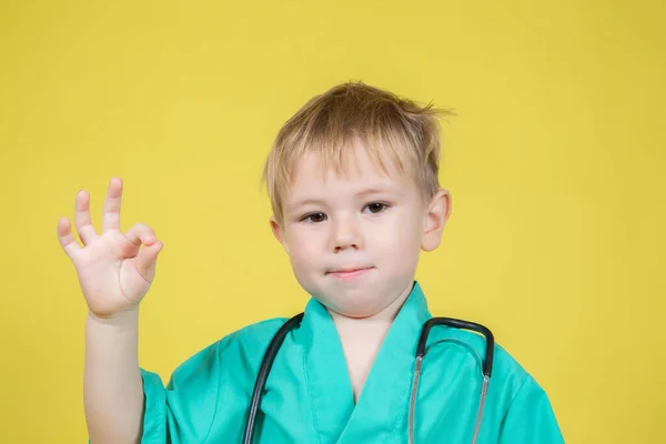 Portrait of little boy dressed in doctors green showing ok gesture — Fotografia de Stock