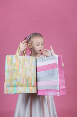 Pembe arka planda parti elbisesi giymiş beyaz bir kız alışveriş torbası tutuyor.