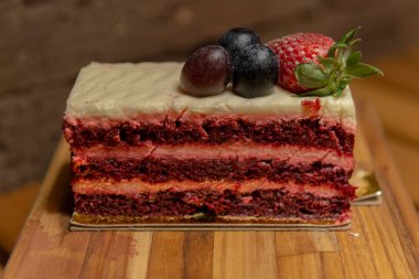 Üzümlü ve ahşap tepside çilekli Lezzetli Kırmızı Kadife kek ve arka planda kırsal tuğla duvar kompozisyonu. Bir dilim lezzetli ve güzel pasta. Seçici odak.