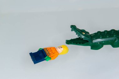 Bauru, Brazil. 7, June, 2022: Top view of Lego minifigure of Aquaman angry swimming belly up with big fierce crocodile in his pool on white background. Space area. Minifigure are made by Lego Group