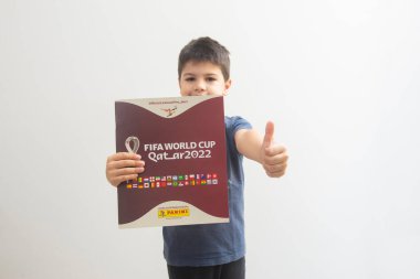 Bauru, Brezilya - 12.09.22: Gülümseyen ve elinde Katar 2022 dünya kupası albümü olan tatlı bir çocuğun ön görünümü - FIFA ve başparmaklar yukarı. Kupa çıkartmaları dünyanın her yerinden insanlar tarafından toplanıyor. Seçici odak.