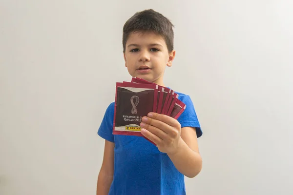 Bauru, Brezilya - 09.12.22: Katar 2022 dünya kupası paketlerini tutan sevimli mutlu çocuk - FIFA. Kupa kartı albümü tüm dünyada milyonlarca insan tarafından toplanıyor. Seçici odak.