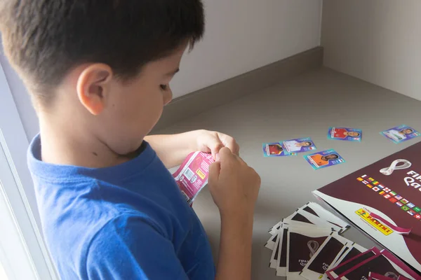 Bauru, Brezilya - 12.09.22: Erkeklerin Panini Fifa Dünya Kupası 2022 - Katar dergilerine yapıştırmak için çıkartma paketleri açması. Dünya Kupası takımlarından oyuncuların koleksiyon etiketleri - FIFA