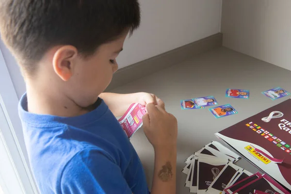Bauru, Brezilya - 12.09.22: Erkeklerin Panini Fifa Dünya Kupası 2022 - Katar dergilerine yapıştırmak için çıkartma paketleri açması. Dünya Kupası takımlarından oyuncuların koleksiyon etiketleri - FIFA