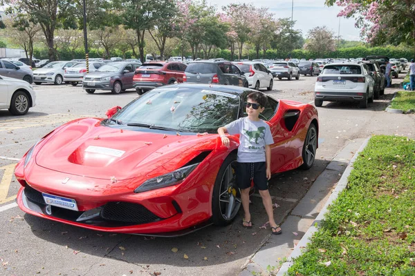 Atibaia - Brezilya, 7 Ekim 2022: Güneş gözlüklü çocuk park halindeki kırmızı Ferrari F8 Haraçlarının yanında poz veriyor. Orta motorlu arka sürücü spor araba. Ferrari - İtalyan lüks spor arabası Maranello, İtalya merkezli