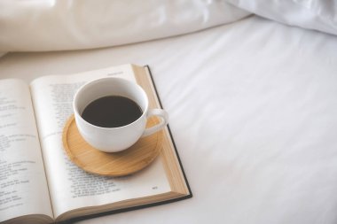 Yatak odasındaki beyaz çarşafların üzerinde bir fincan kahve. Sabah yaşam tarzı konsepti.