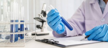Bilim adamı ilaç laboratuvarında temiz çözeltiye sahip test tüpünü inceliyor..