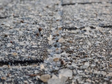 Kışın buzlu kaldırım yüzeyinde tuz taneleri. Yolları açık tutmak için tuz uygulamak ve kış mevsiminde insanları buzdan ve kardan korumak, yakın görüş