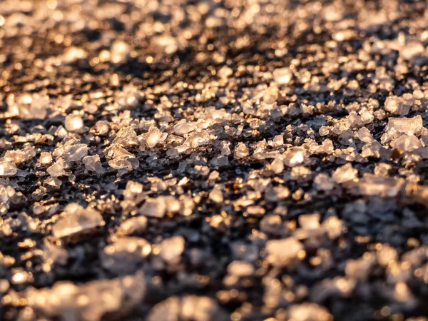 冬の氷の歩道表面の塩粒 氷や雪から冬の天候で道路をクリアし 人々を安全に保つために塩を適用します 冬の太陽の下での塩粒のマクロビュー — ストック写真