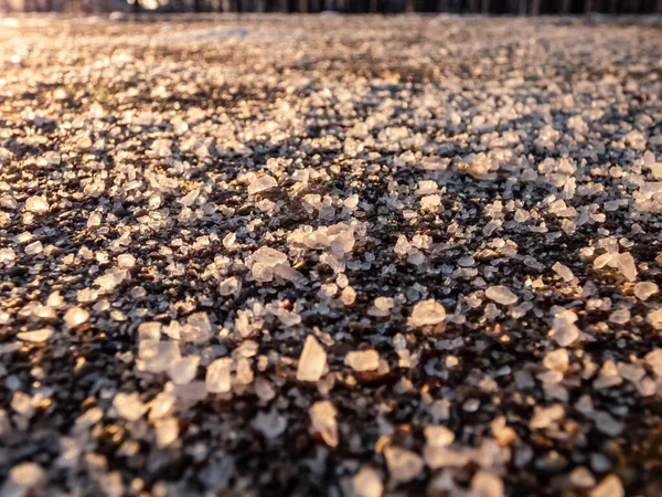 冬の氷の歩道表面の塩粒 氷や雪から冬の天候で道路をクリアし 人々を安全に保つために塩を適用します 冬の太陽の下での塩粒のマクロビュー — ストック写真