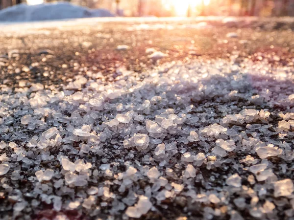 冬の氷の歩道表面の塩粒 氷や雪から冬の天候で道路をクリアし 人々を安全に保つために塩を適用します 冬の太陽の下での塩粒のマクロビュー — ストック写真