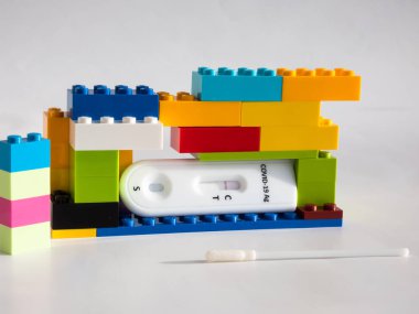 SARS-CoV-2 Antijen Hızlı Testi (nazal Swab), beyaz üzerine kenetlenmiş oyuncak tuğlaları arasında negatif sonuç veren bir çubuk ve test kaseti ile kendini test etmek için. COVID-19 Ag. Çocukluktaki salgın kavramı