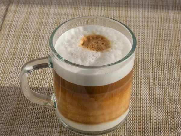 ホットカプチーノコーヒーをグラスマグカップに閉じ込めて コーヒーカプセルで作られたテーブルの上に泡蒸しミルクとエスプレッソの層があります — ストック写真