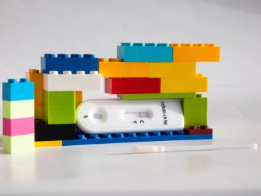 SARS-CoV-2 Antijen Hızlı Testi (nazal Swab), beyaz üzerine kenetlenmiş oyuncak tuğlaları arasında negatif sonuç veren bir çubuk ve test kaseti ile kendini test etmek için. COVID-19 Ag. Çocukluktaki salgın kavramı