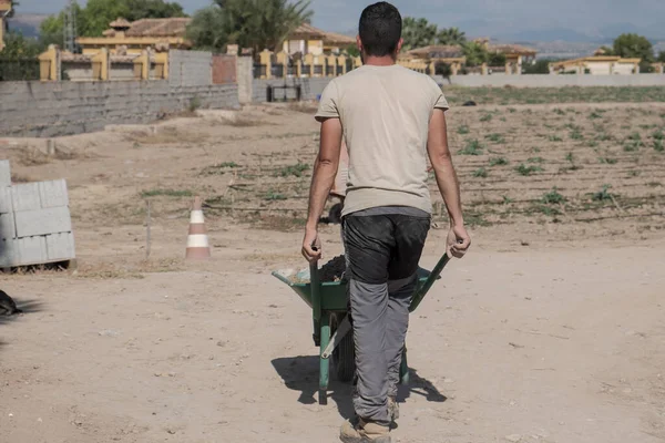 Sırtı el arabasıyla mal taşıyan genç bir işçi. Çaba kavramı.