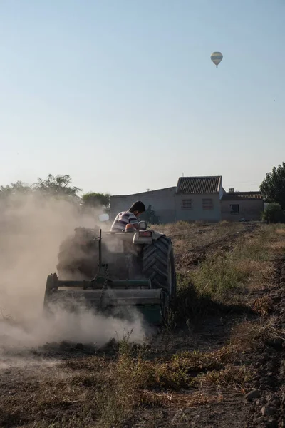 Genç çiftçi bir traktörle tarlada çalışıyor sıcak hava balonuyla gökyüzünde seyahat ediyor.