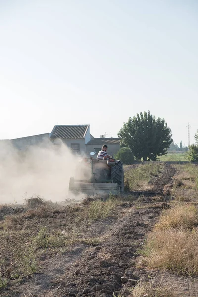 Genç çiftçi, toza bulanmış traktörüyle toprağı sürüyor.