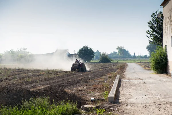 Genç çiftçi traktöründe tarlayı işliyor. Etrafı toz bulutuyla çevrili.