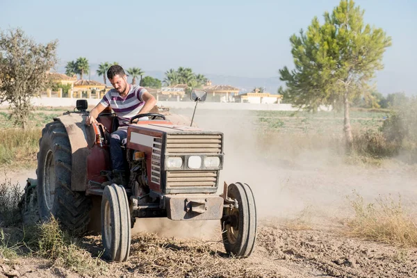 young farmer ploughing the field in his tractor surrounded by a cloud of dust