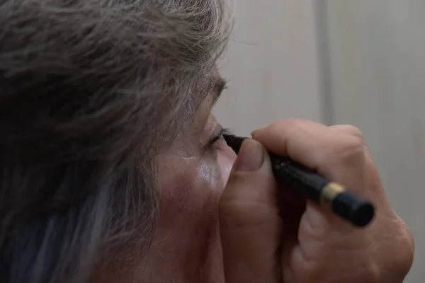 Yetişkin bir kadın makyaj yapıyor ve göz hizasını evdeki tuvalete boyuyor..