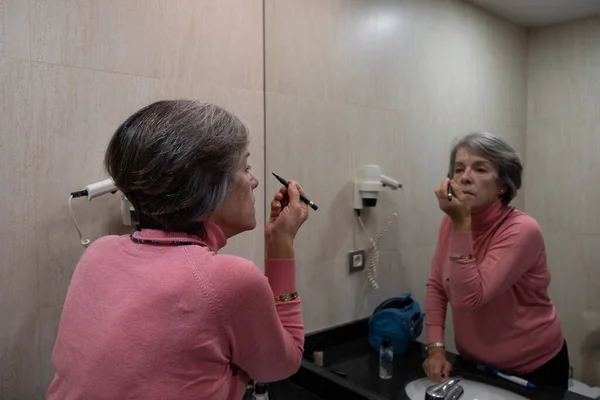 50 yaşında bir kadın aynanın karşısına makyaj yapmaya hazırlanıyor. Güzellik konsepti.