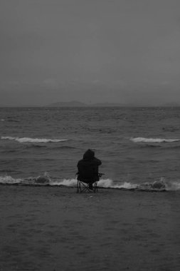 Sahildeki bir adamın siyah beyaz fotoğrafı.