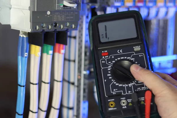 An electrical engineer measures the parameters of electrical circuits using a multimeter in the control panel.