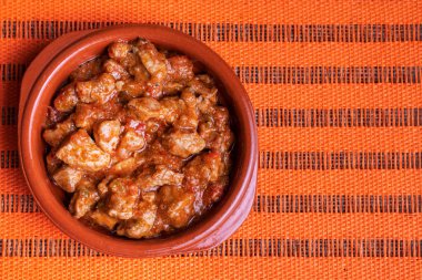 Turuncu masa örtüsü üzerinde domatesli çamur tabağı dolusu et..