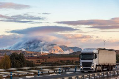 Arka planda bulutlarla çevrili dağlarla otoyolda karavan gezintisi..