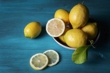 Limonlar bir kasede ve iki dilim dilimler, hepsi açık mavi ahşap bir masada..