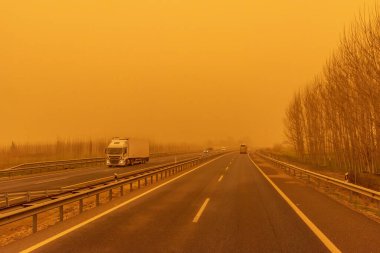 Sahra kum fırtınası gününde (kalima) dolaşan soğutmalı bir kamyonla otoyol manzarası sarımsı bir ortam yaratıyor..