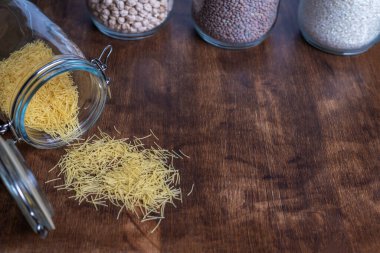 Etrafı sebzeli tencerelerle çevrili, ahşap bir masaya saçılmış erişteli çömlek..