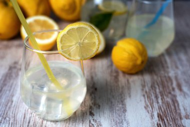 Limonata ve buzlu bardak, kenarında bir dilim limon, arka planda bir sürahi ve odak limonları..