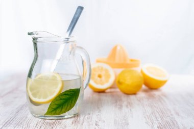 Limonata ve küp sürahi, bir dilim limon ve yeşil yaprak, arka planda biraz limon ve odak dışı bir sıkma..