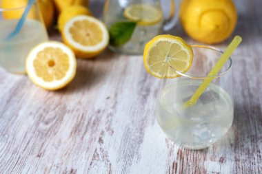 Limonata ve buzlu bardak, kenarında bir dilim limon, arka planda bir sürahi ve odak limonları..