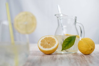 Limonatalı sürahi ve limonların yanında yeşil bir yaprak. Bir dilim limonata ile bulanık bir ön plan..