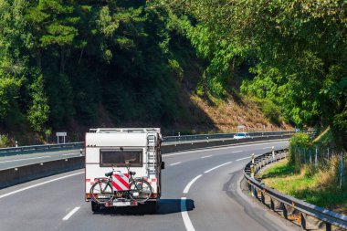 Motorhome with a bicycle behind driving on a highway surrounded by trees