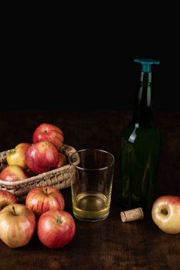 Bottle of cider with a stopper to pour next to a glass with cider and some apples.