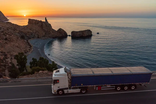 Truck with dump body driving along a road by the sea.