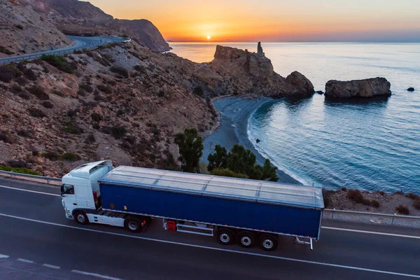 Truck with dump body driving along a road by the sea.